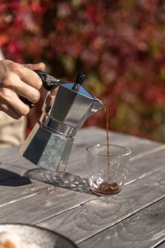 秋天，在户外乡村的桌子上，用手将咖啡从摩卡壶倒入玻璃杯