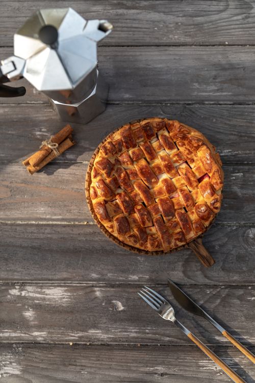 Free A top-down view of a rustic pie on a wooden table with a coffee maker and cinnamon sticks. Stock Photo