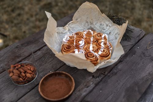 Free Freshly baked cinnamon rolls on parchment paper with a side of almonds and cinnamon powder. Stock Photo