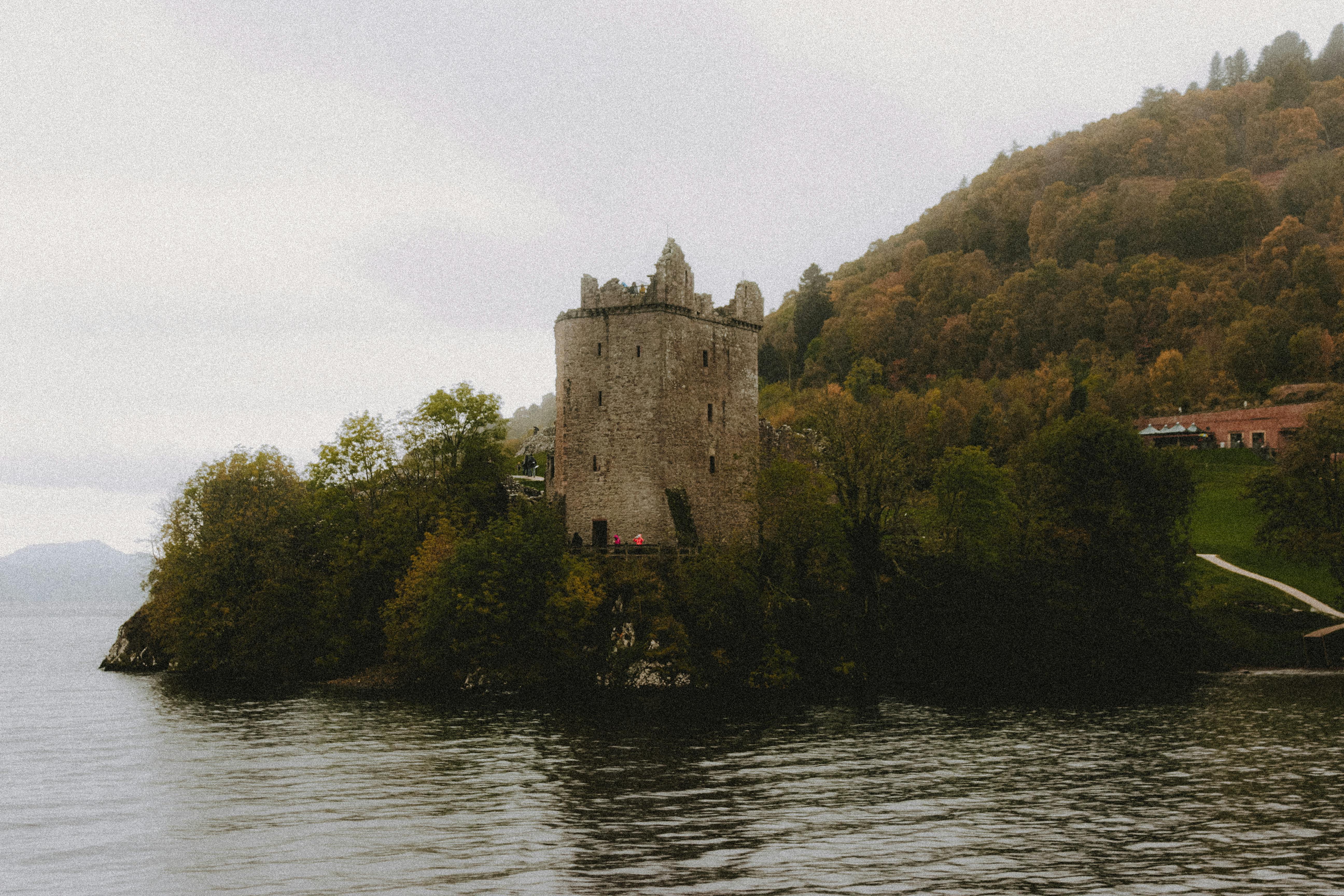 medieval tower facade on green ridge near lake in fog
