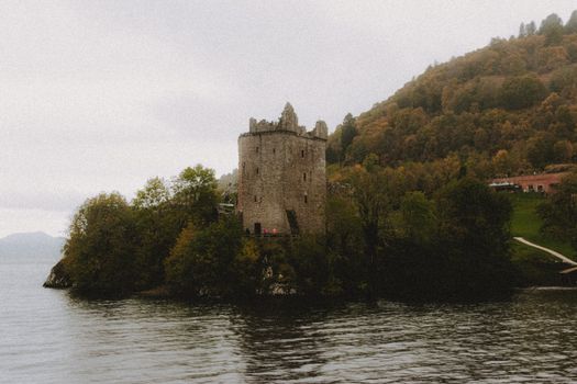 Scenic view of ancient masonry castle exterior on mountain with trees near Loch Ness lake under misty sky