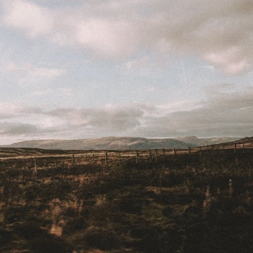 Fenced pathway in mountains under cloudy sky