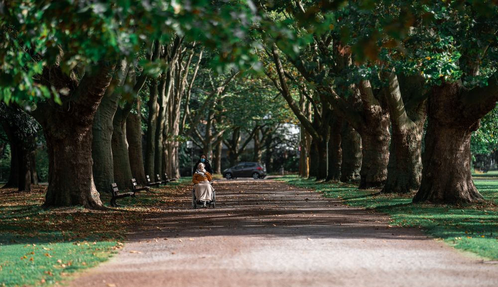 A caregiver walking outdoors with a senior woman in a wheelchair