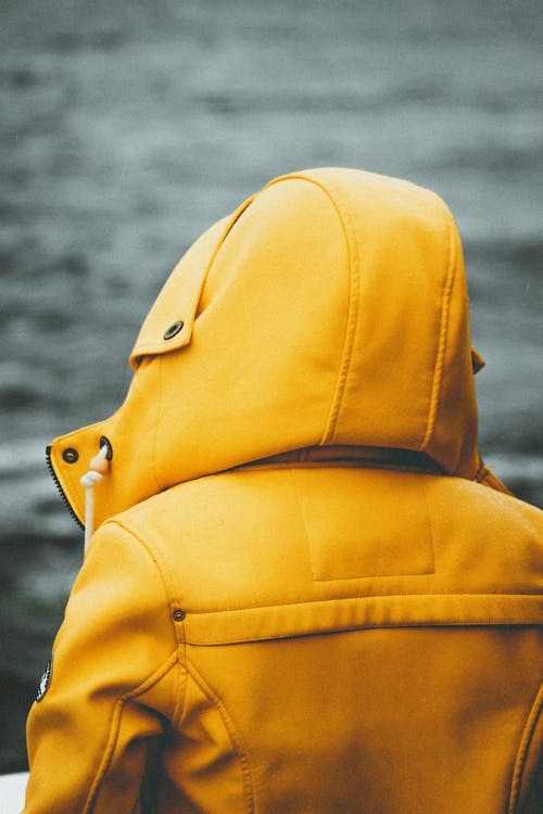 Anonymous tourist in yellow outerwear contemplating sea