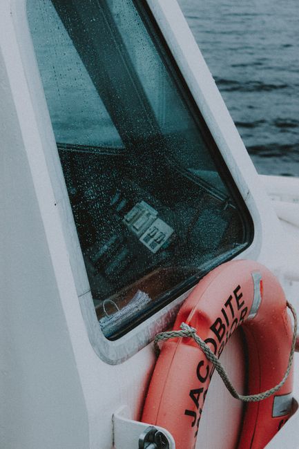 Modern yacht with bright life ring tied with rope near wet cabin glass on rippled ocean in rainy weather