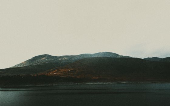 Picturesque view of rough ridges with trees near ocean under cloudless sky in evening