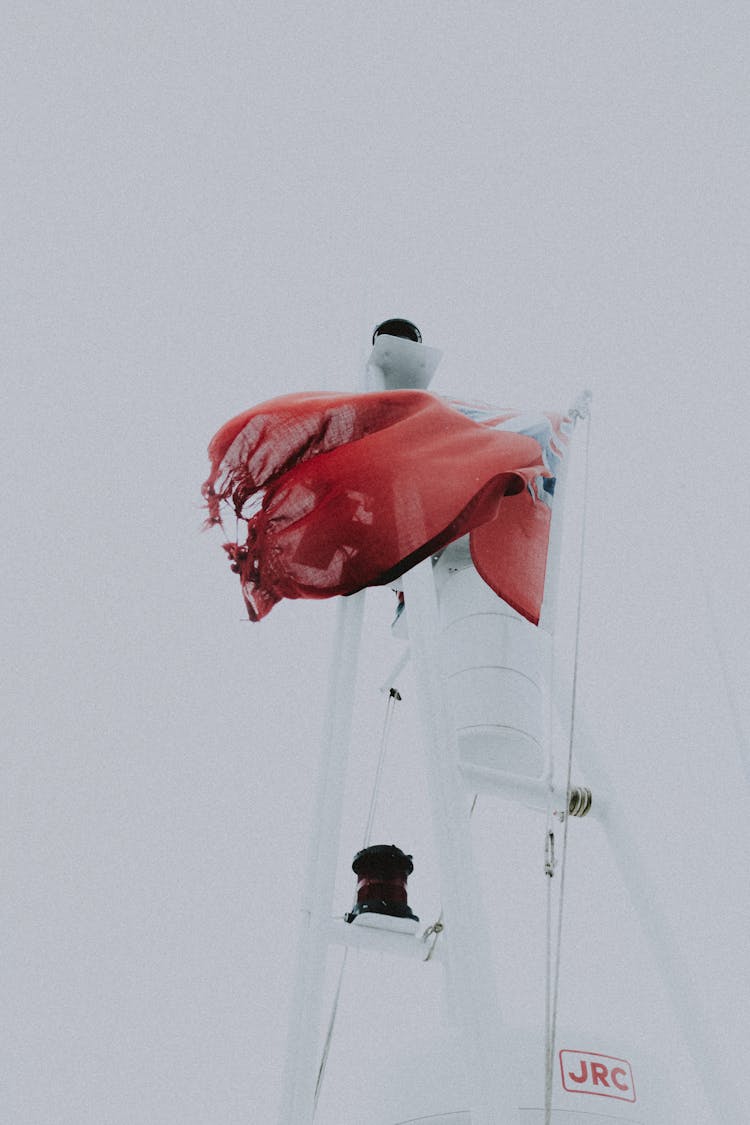 Bright Flying Flag On Mast Of Yacht Under White Sky