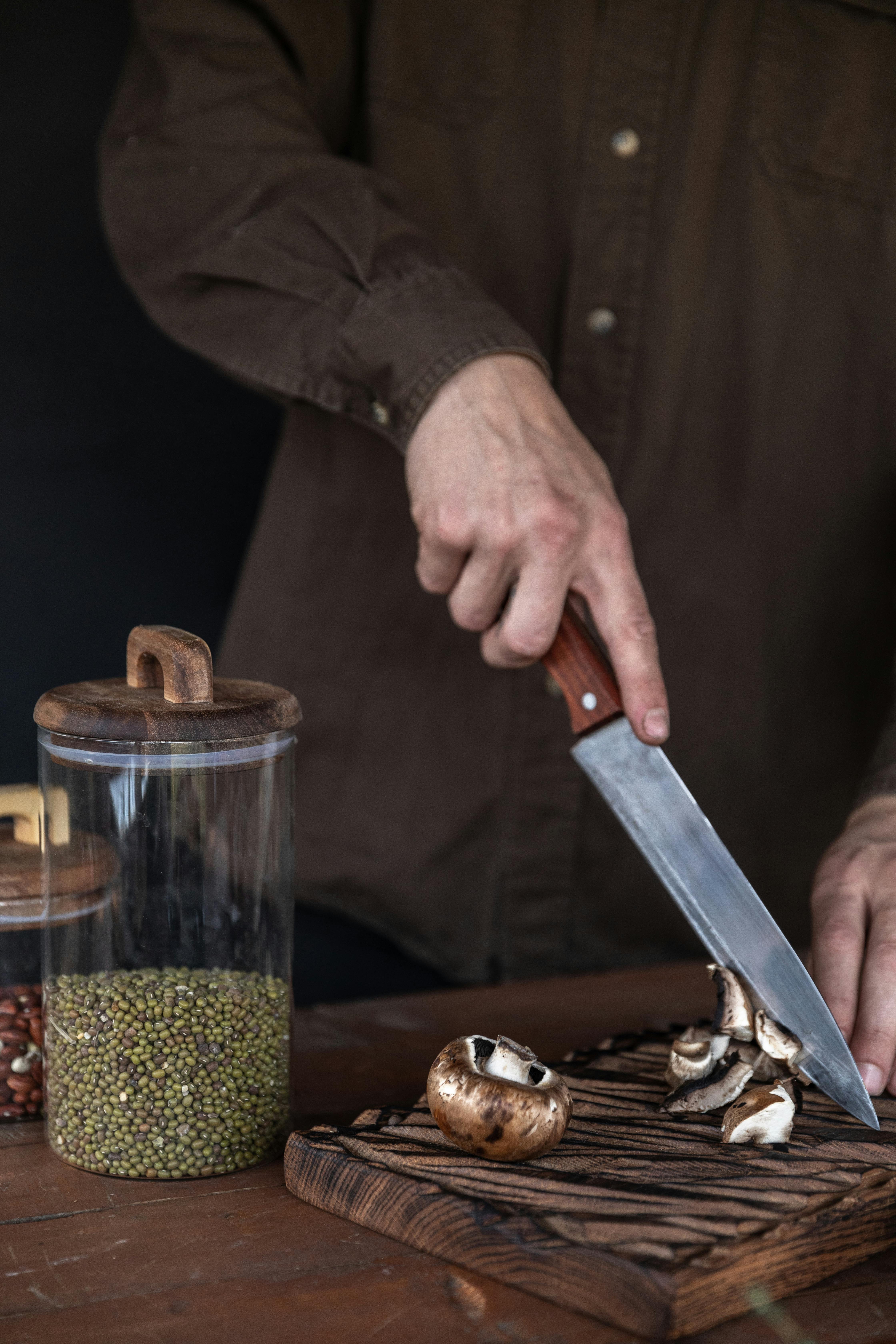 person holding a knife and slicing mushrooms in a wooden chopping board