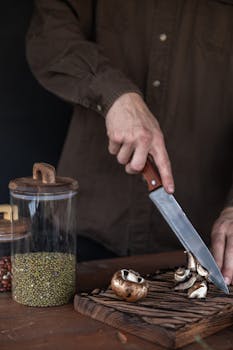 A person slicing mushrooms on a wooden chopping board beside a glass container of mung beans.