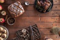 A rustic top-down view of a Thanksgiving spread with bread, roasted turkey, and apples on a wooden table.