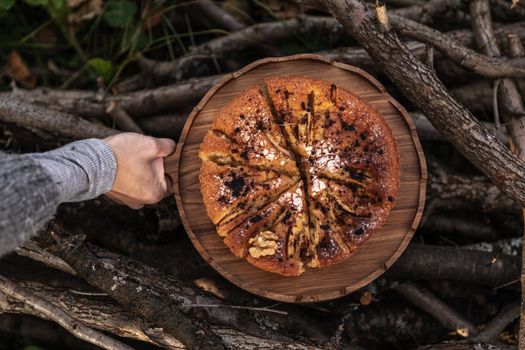 Top view of a delicious cake with walnuts on a wooden tray, held outdoors among branches.