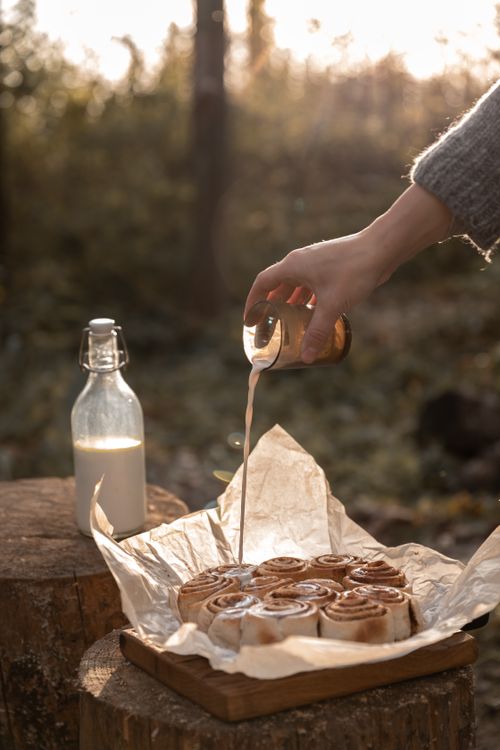 Free Freshly baked cinnamon rolls being drizzled with glaze outdoors in warm light. Stock Photo
