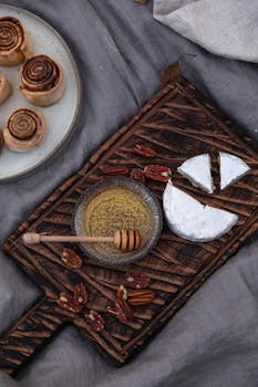 A rustic display of cheese, honey, pecans, and pastries on wooden board.