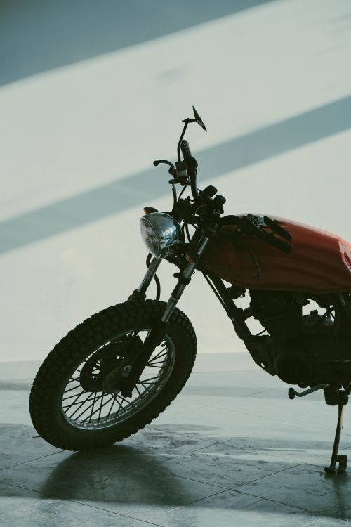 Free Close-up view of a vintage motorcycle parked in a sunlit indoor space, casting long shadows. Stock Photo