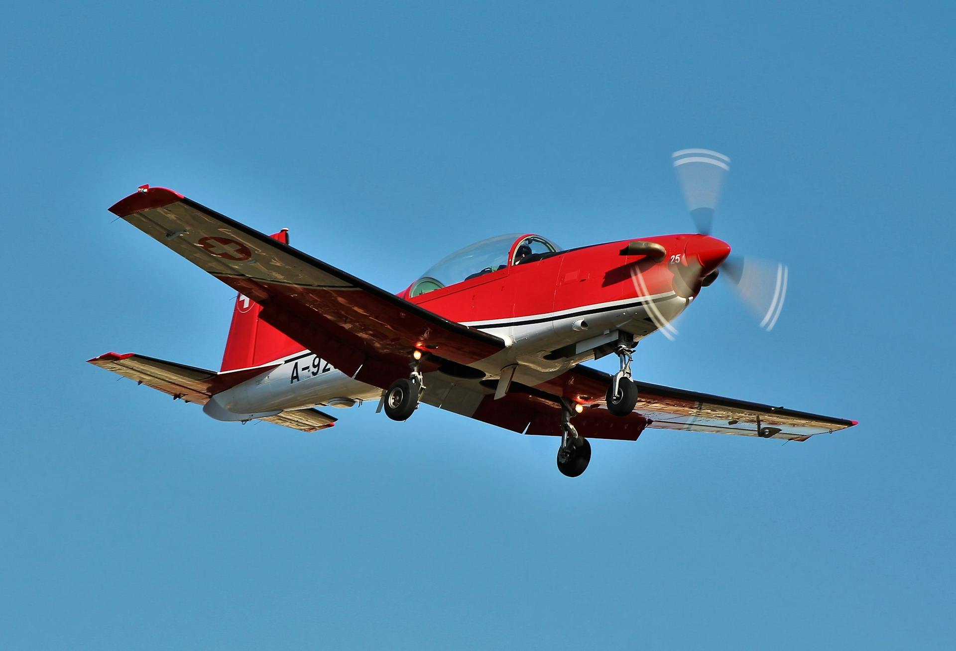 Dynamic shot of a red turboprop plane flying against a clear blue sky.