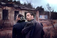 两名身穿军装的男子在废弃建筑物附近户外吸烟