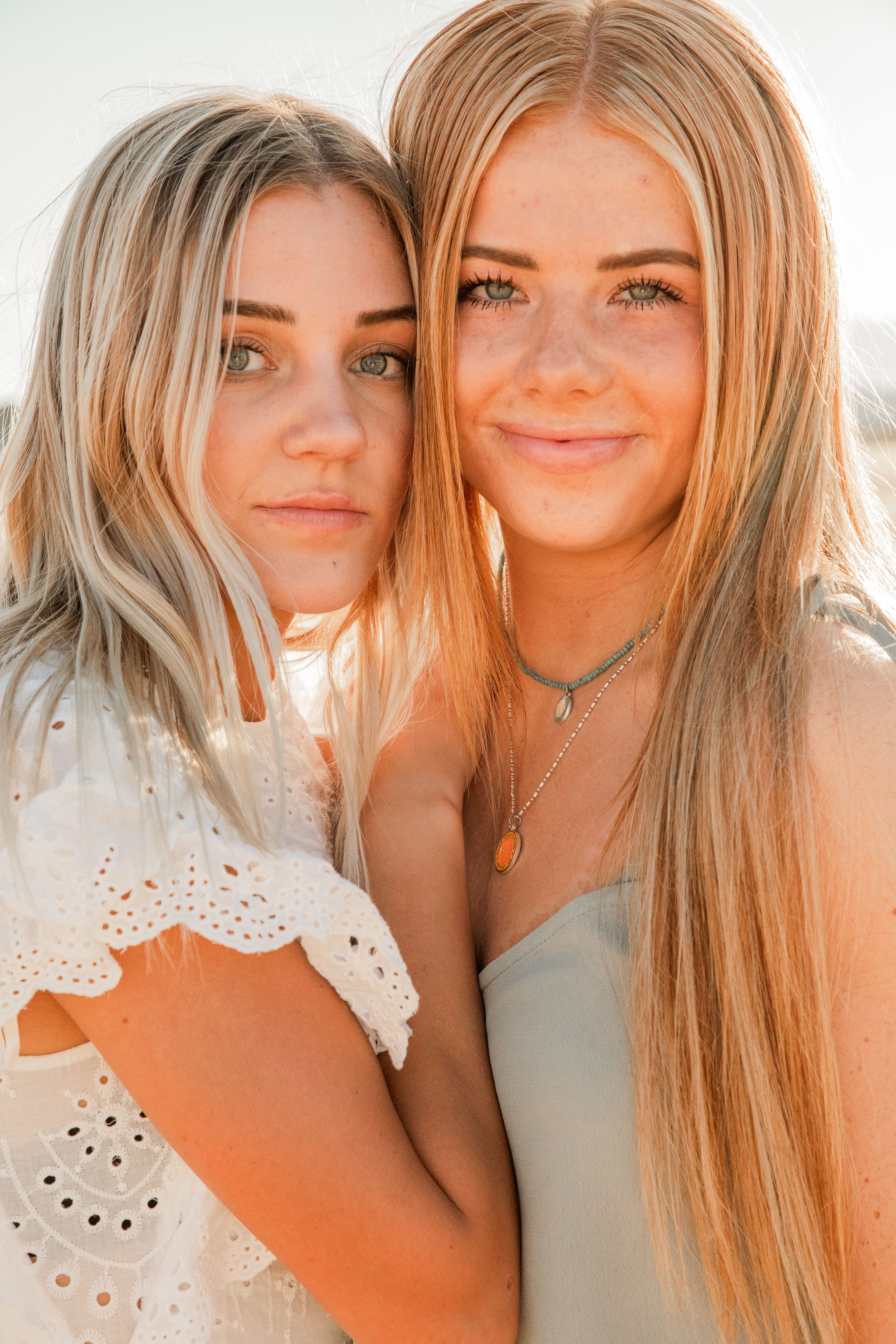 Young attentive woman in trendy wear standing close to crop content girlfriend in accessories while looking at camera in back lit