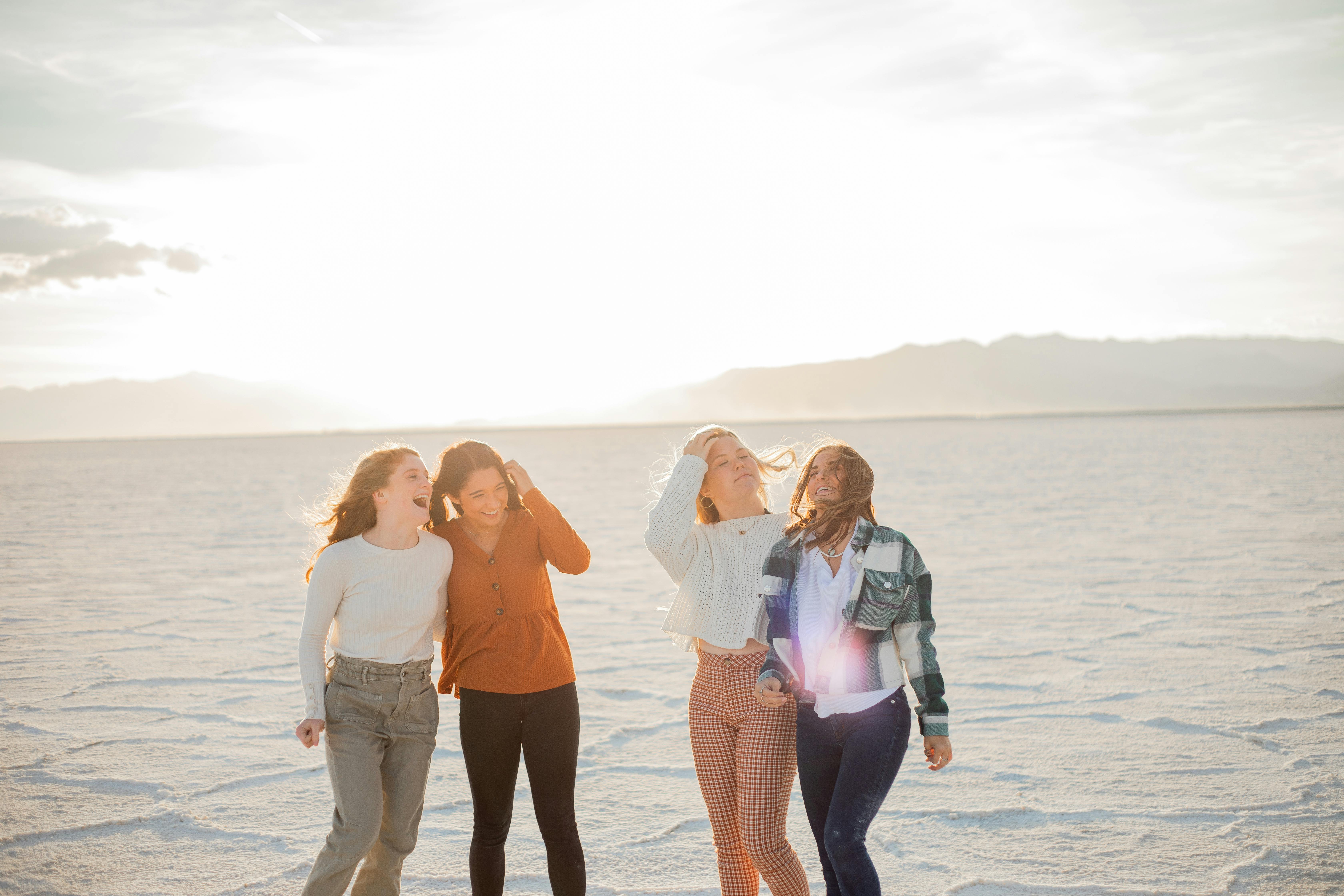 excited girlfriends in trendy wear in desert under shiny sky