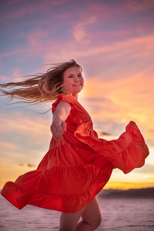 Smiling woman in flying red dress at sunset