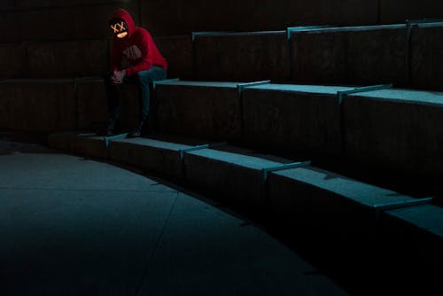 A Man in Red Hoodie Sitting on Concrete