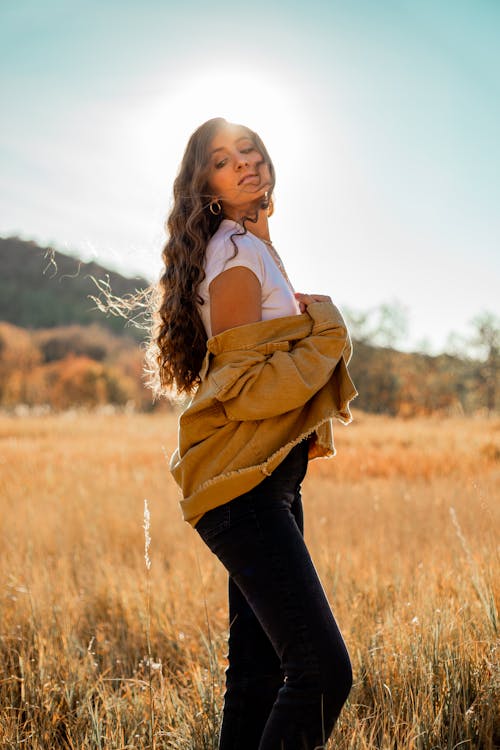 Low angle side view of young contemplative stylish lady on grass meadow looking away in back lit