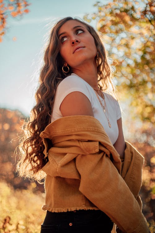 Side view of young contemplative female with wavy hair looking away over shoulder in fall in back lit