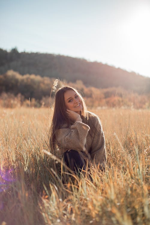 Charming trendy woman in field among grass in sunshine