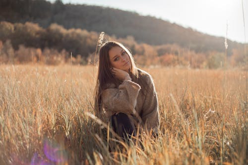 Free Woman in Brown Sweater Sitting on Brown Grass Field Stock Photo