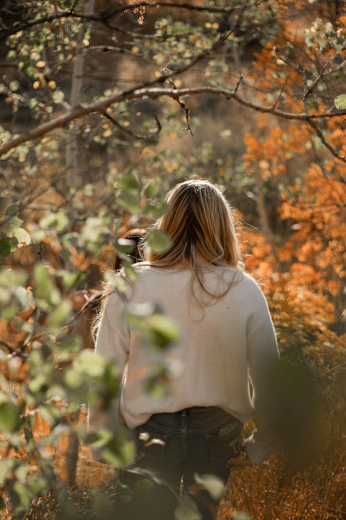 Woman in White Long Sleeve Shirt Standing Near Brown Leaf Tree