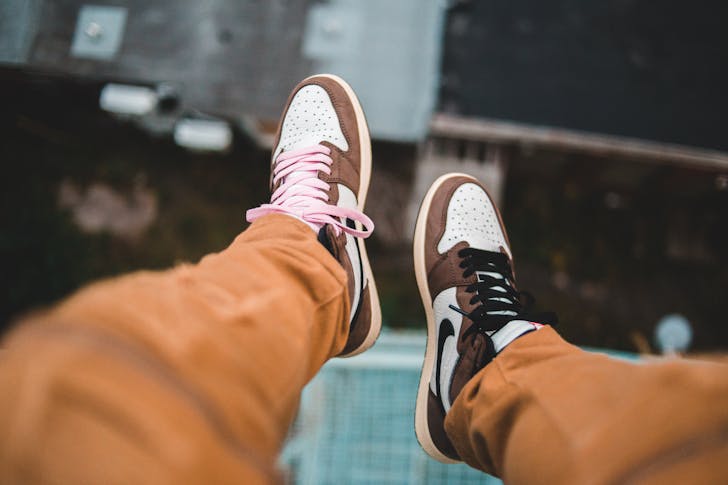 From above of male feet in sneakers with different shoelaces above blurred street at height