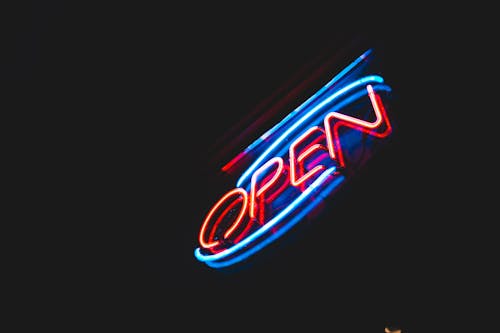 From below of Open sign with colorful neon lights hanging on building against dark night sky