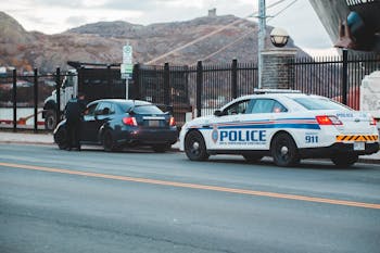 Back view of unrecognizable police officer in uniform checking modern car parked on asphalt road against cloudy sky