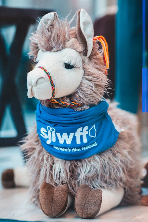 Adorable soft plush lama toy placed on parquet floor at home in daylight