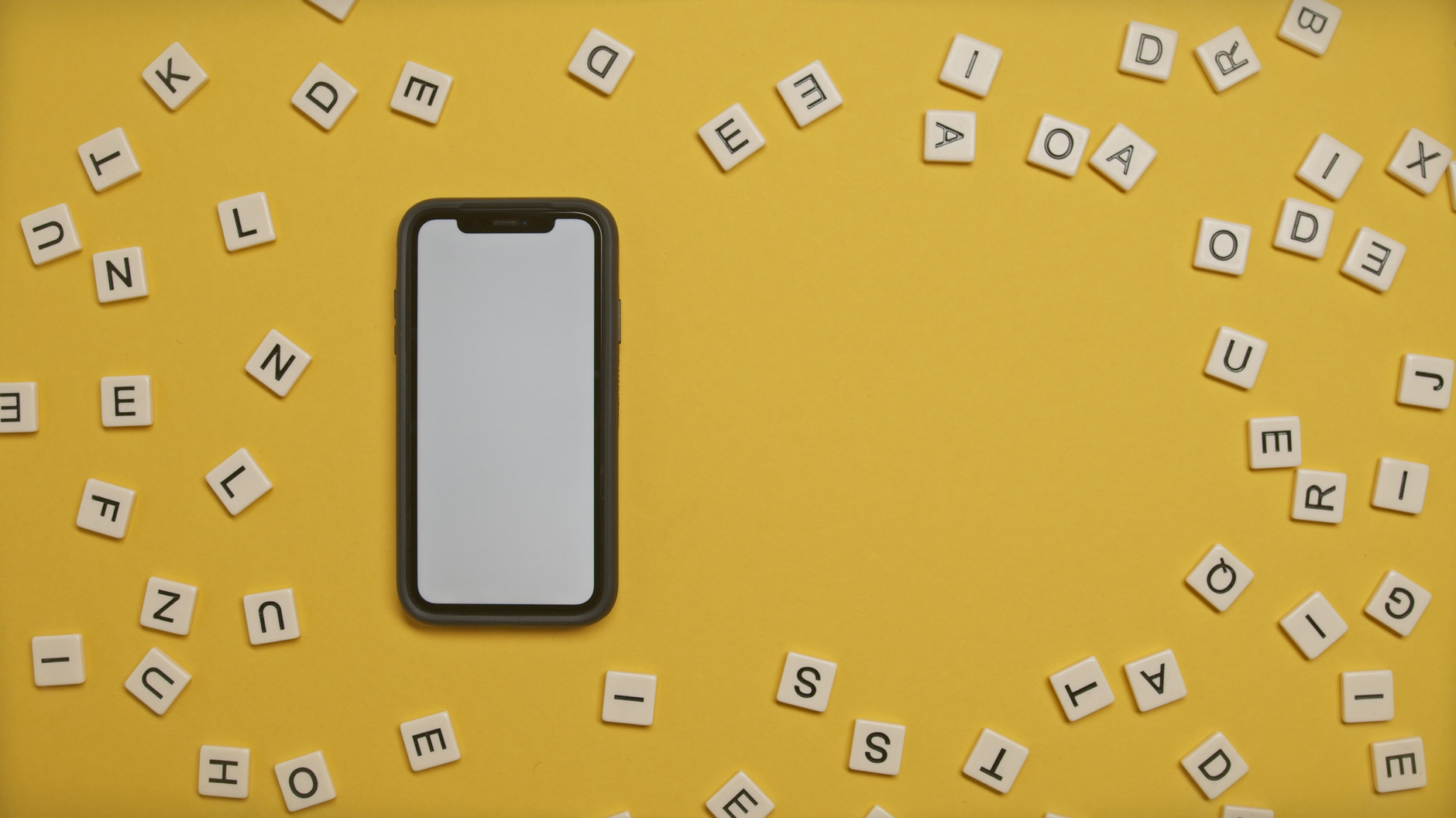 Smartphone surrounded by scattered alphabet tiles on a vibrant yellow background.