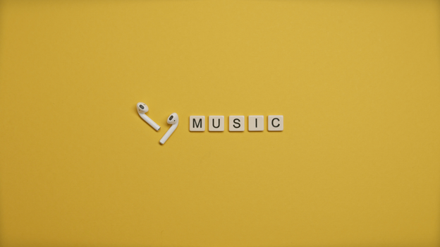 Minimalist image of AirPods and music-themed letter tiles on a vibrant yellow background.