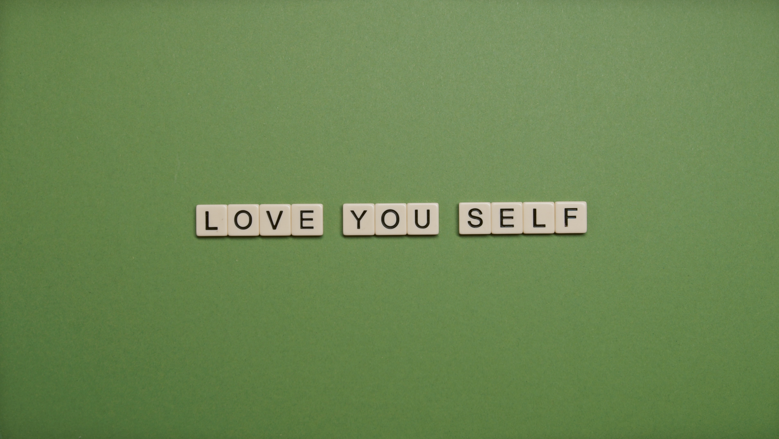 Positive message 'Love You Self' spelled with letter tiles on green background.