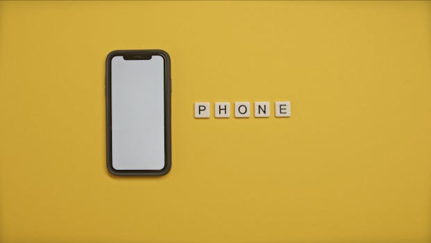 Flat lay of smartphone and 'PHONE' letter tiles on vibrant yellow background.