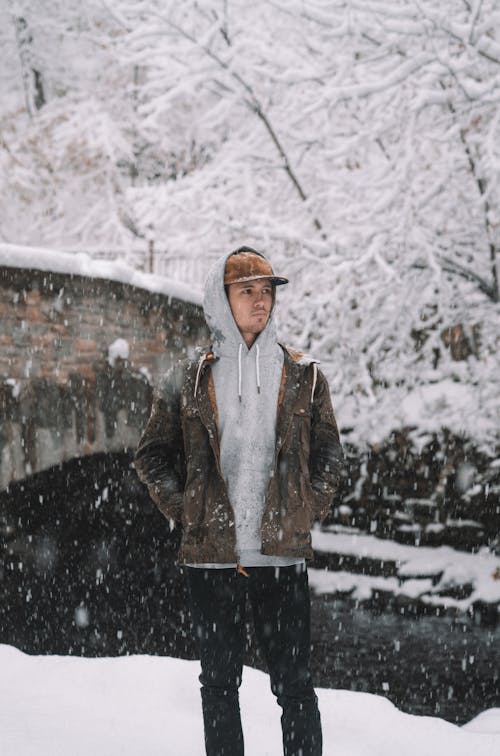 Adult man in hoodie and jacket standing in nature in heavy snowfall and looking away