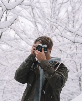 一个穿着暖和衣服的男人在白雪覆盖的森林中用相机捕捉冬天的场景