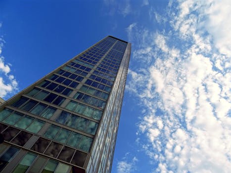 低角度拍摄的现代玻璃摩天大楼，映衬着明亮的蓝天，云层散落