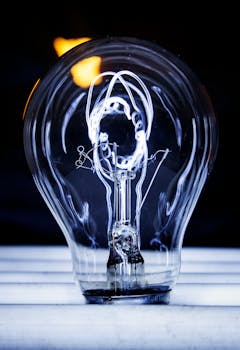 Artistic photo featuring a glowing light bulb with visible filament against a dark background.