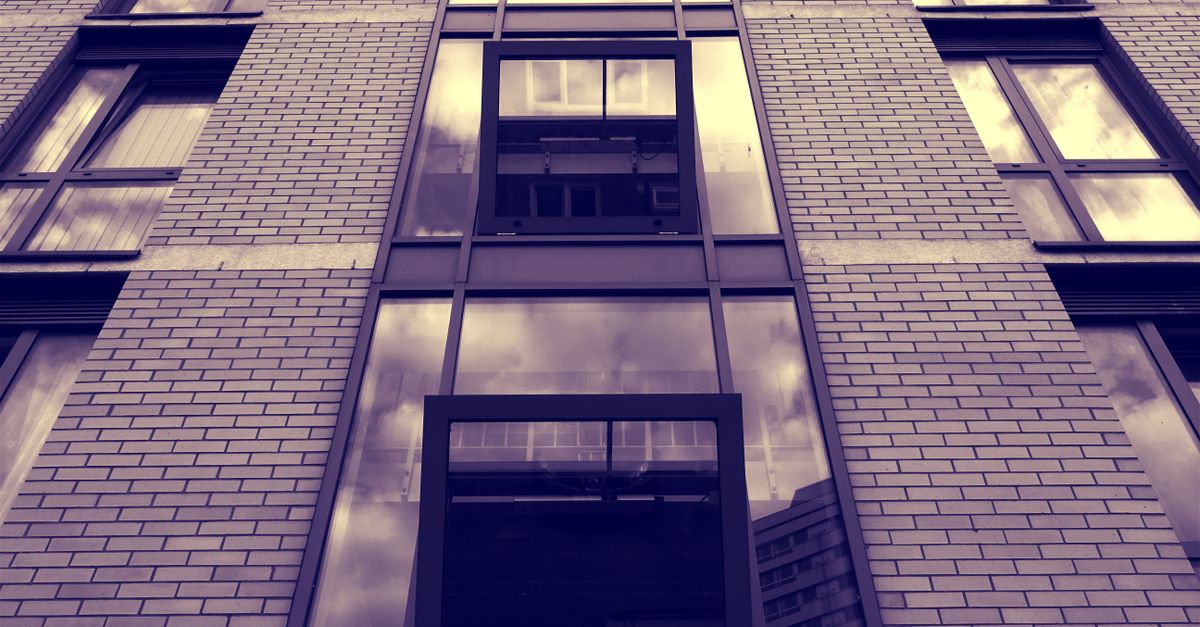 Low-angle view of a modern urban building facade with reflective glass windows and brick walls.