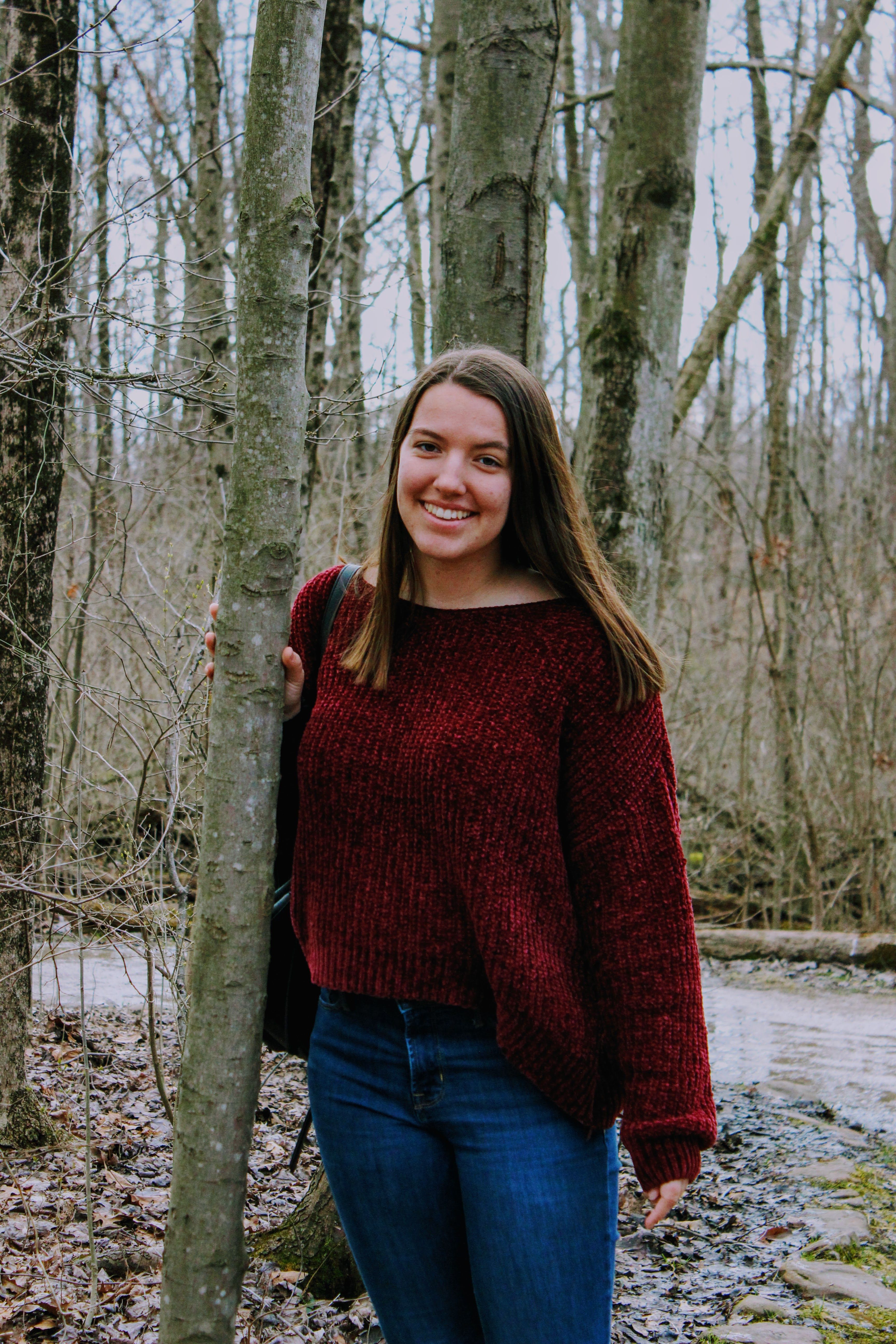 Portrait of a smiling woman standing in a quiet forest, surrounded by trees.