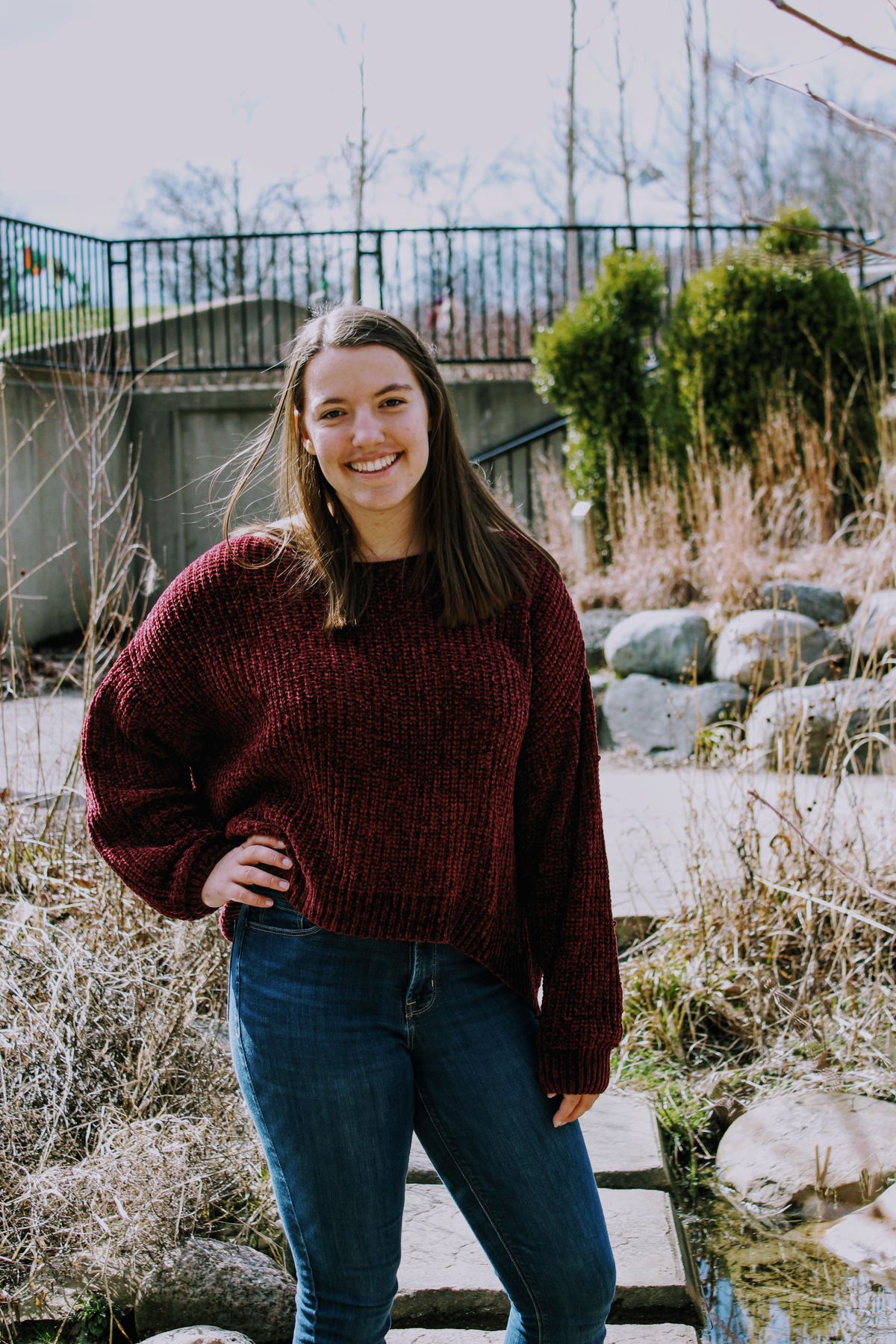 Burgundy Outfits for Women — 7 Wine Red Looks for Fall and Winter Woman in a burgundy sweater and blue jeans outdoors