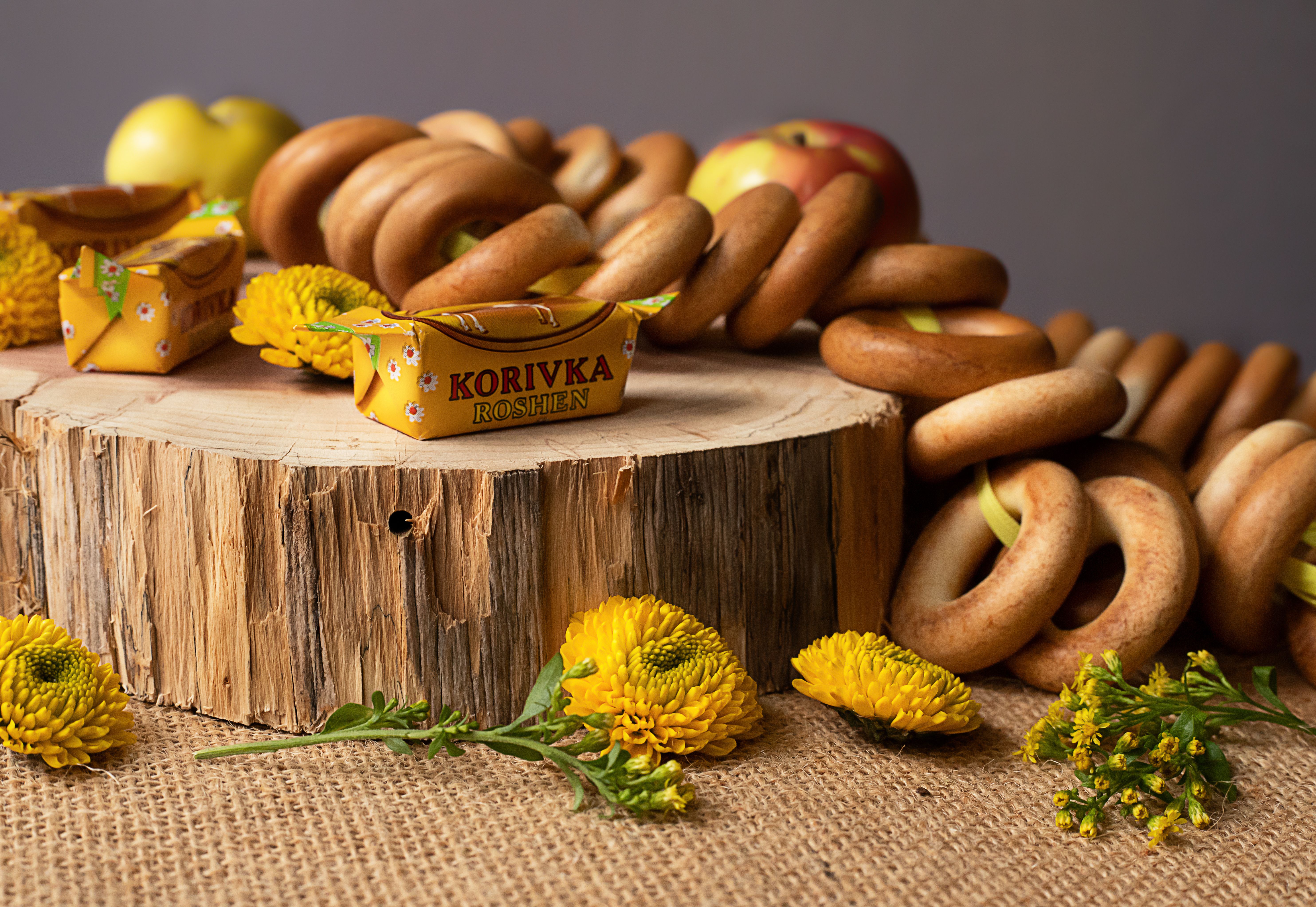 A rustic display featuring bagels, Korivka candies, and yellow flowers on a wood slab.
