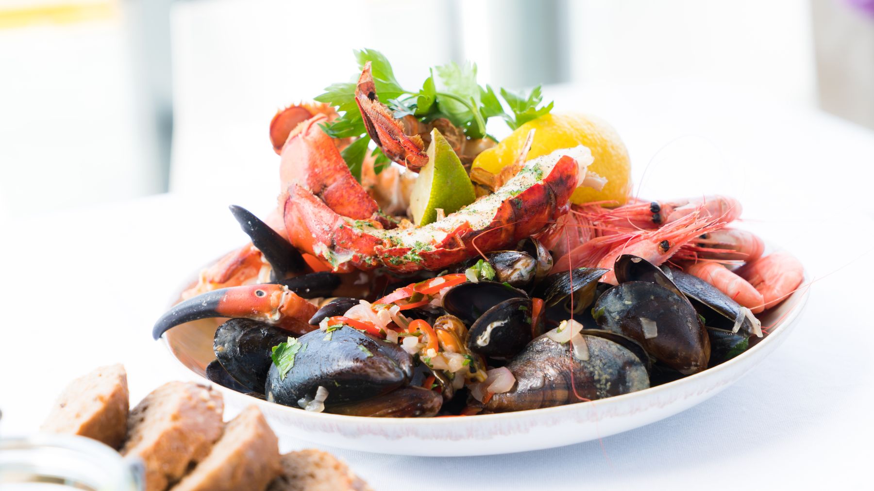 Un vivace piatto di frutti di mare con aragosta, gamberi, cozze e limone su un piatto bianco.