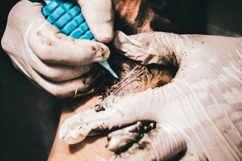 A Person Wearing White Latex Gloves Holding Blue Tattoo Machine