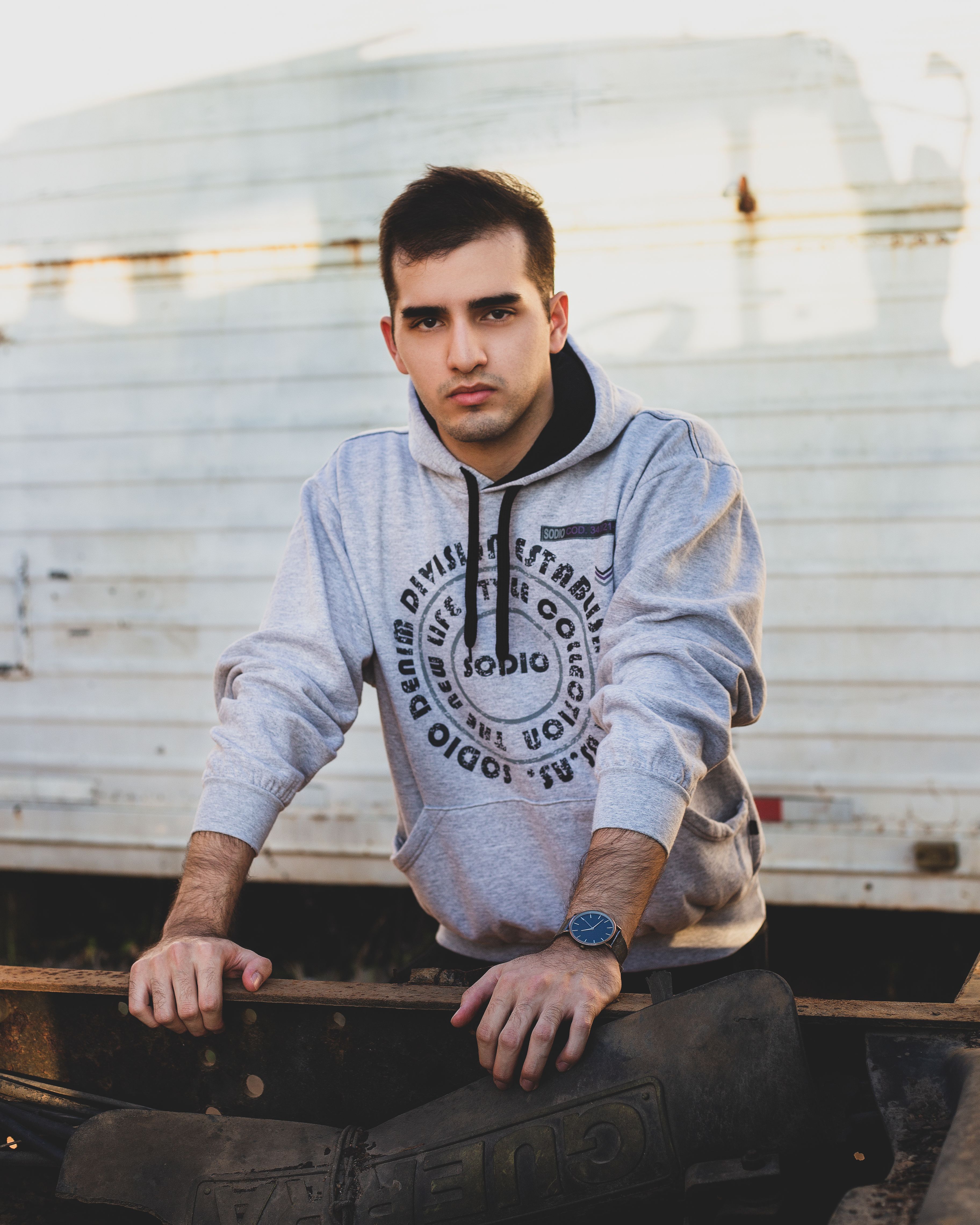 Serious young male in casual clothes standing in street near shabby metal construction and looking at camera in sunny day