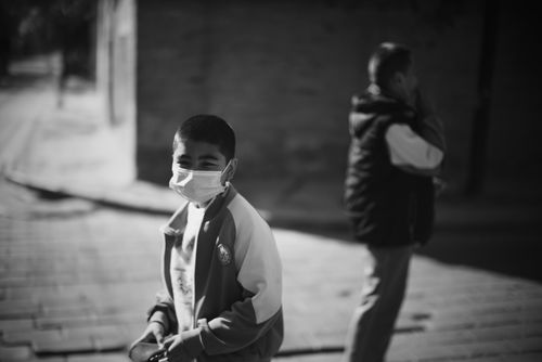Free A young boy in a mask standing on the street in a black and white portrait. Stock Photo