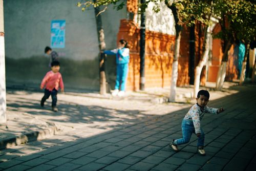 Free Young children playing outside on a sunny urban street with trees and shadows on the pavement. Stock Photo
